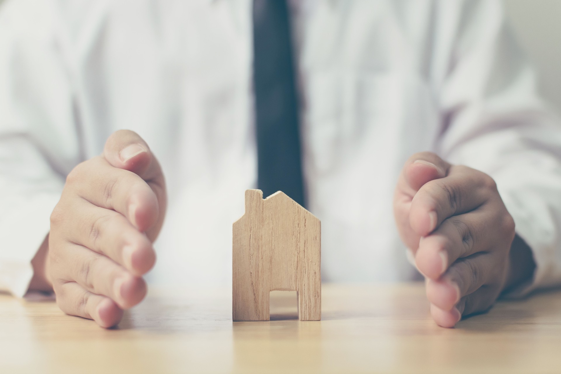 Concetto di protezione della casa assicurativa. Le mani dell'uomo impediscono la casa di legno